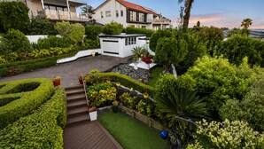 Un immobile residenziale con giardino curato, un patio in legno e un garage bianco.