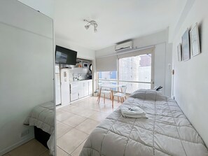 A compact bedroom with a bed, a small kitchenette, a TV, and a window with a view. - Charming Studio Your Urban Retreat in Recoleta Buenos Aires (Buenos Aires)