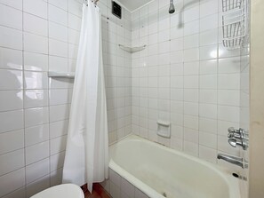 Een badkamer met witte tegels, een bad, een douchegordijn en een toilet.