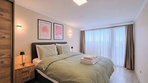 A bedroom with a bed, bedside tables, a lamp, artwork, and a large window with curtains. - Refined 2BR with Terrace and Bosphorus View (Kadıköy)