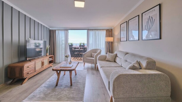 A modern living room with a sofa, a coffee table, a TV, and a dining area with chairs and a table. - Refined 2BR with Terrace and Bosphorus View (Kadıköy)