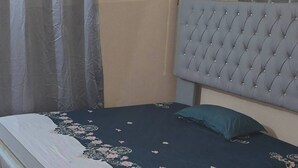 Ein Bett mit einem gebügelten Kopfteil, einer floralen Tagesdecke und einem grauen Vorhang.