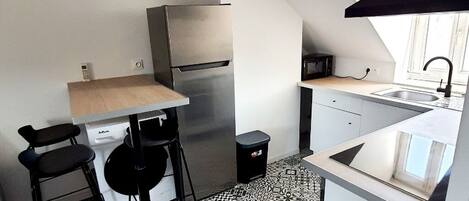 Una cocina compacta con refrigerador, microondas, lavamanos y un ventanal pequeño.
