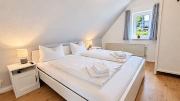 A bedroom with a large bed, two bedside tables, a nightstand, a window with curtains, and a radiator.