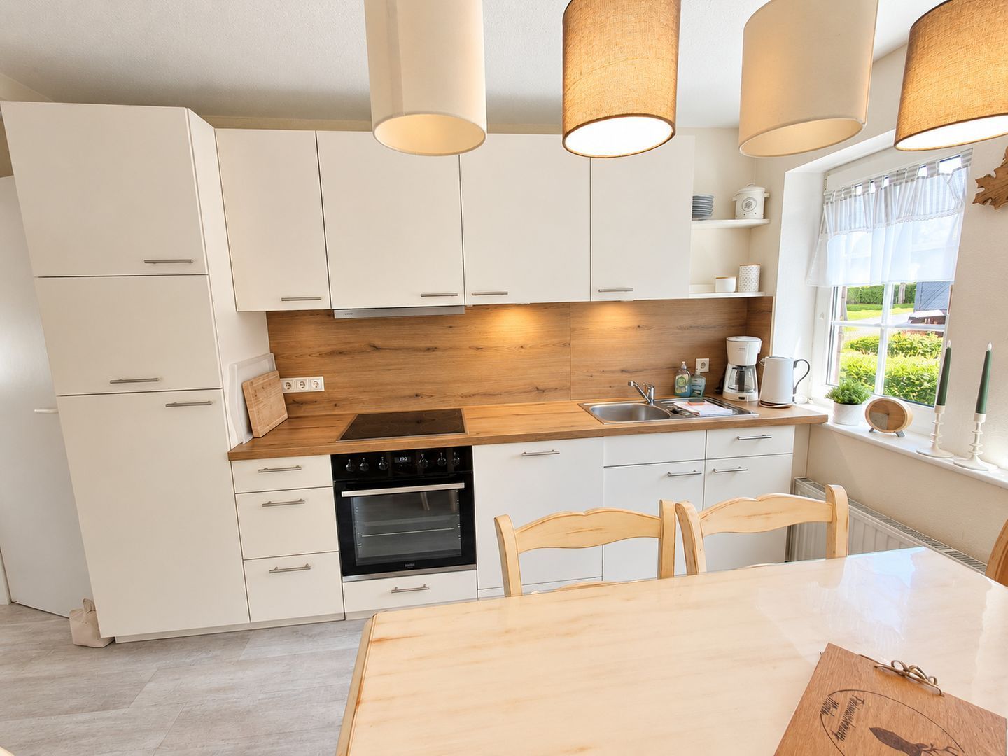 Une cuisine moderne avec des armoires blanches, un plan de travail en bois, un four encastré et une table à manger avec des chaises.