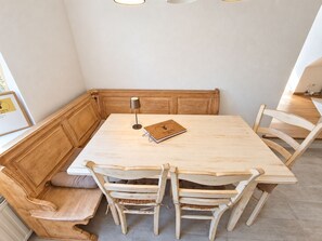 Una zona de comedor en esquina con una mesa y banco de madera, una lámpara y un cuaderno.