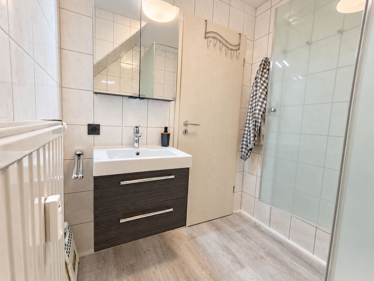 A bathroom with a white sink, dark wood cabinet, and a glass shower enclosure.