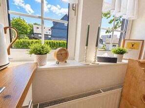 Una cocina con vista al exterior, un hervidor, un reloj y dos plantas en macetas.