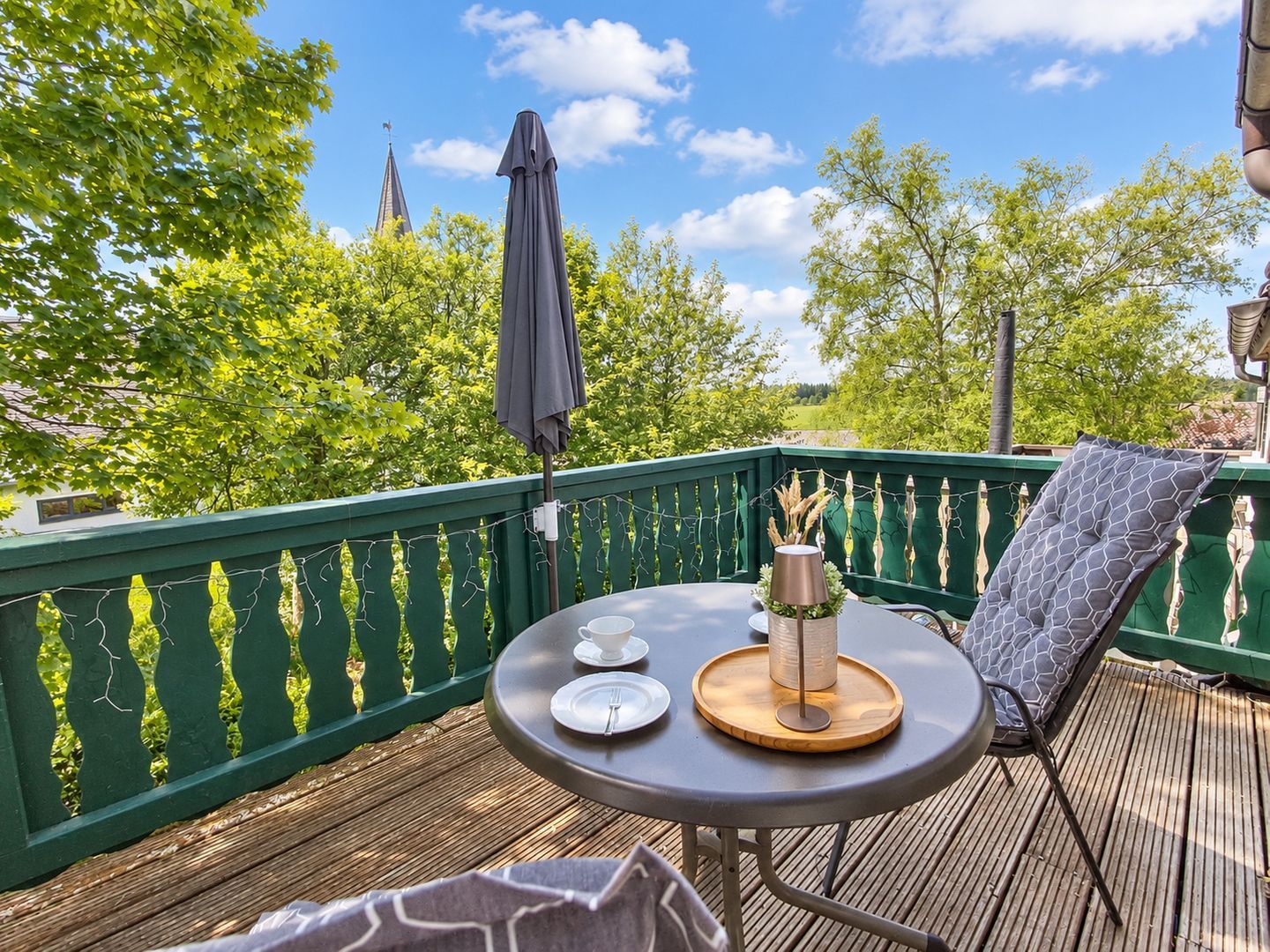 A wooden deck with a table set for two, a chair, and a green railing.