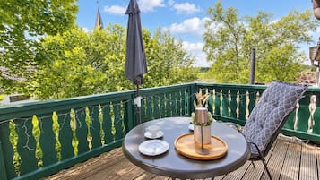 A wooden deck with a table set for two, a chair, and a green railing.