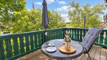 Terraza de madera con una mesa lista para dos personas, una silla y baranda verde.