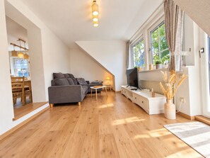 Una sala moderna con sofá, televisor y comedor con muebles de madera.