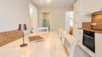 A modern kitchen with a wooden dining table, white chairs, and a built-in oven.