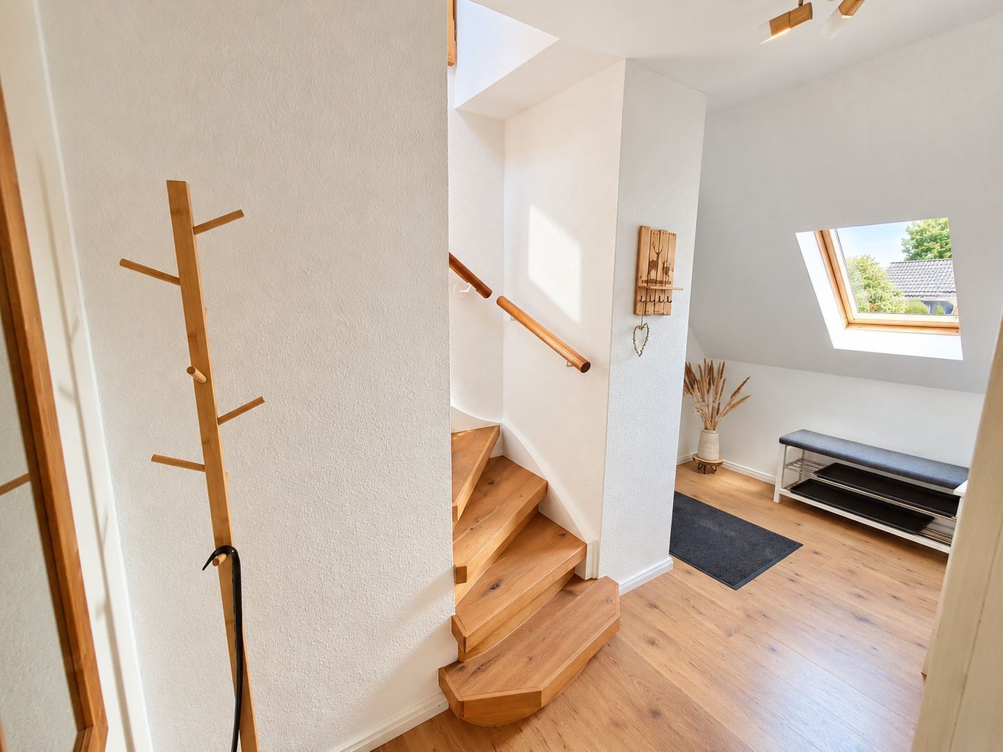Un escalier avec des marches en bois et une rampe, menant à une pièce dotée d’une lucarne et d’un banc.