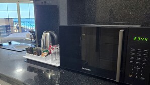 Een keuken met een zwarte magnetron, een koffieapparaat en een digitale klok waarop 23:44 staat.