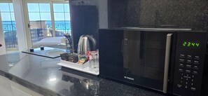 Eine Küche mit einer schwarzen Mikrowelle, einer Kaffeemaschine und einer digitalen Uhr, die 23:44 anzeigt.