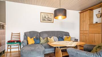 Un salon chaleureux avec un canapé gris, un pouf et un fauteuil assortis, une table basse en bois et un tapis à motifs.