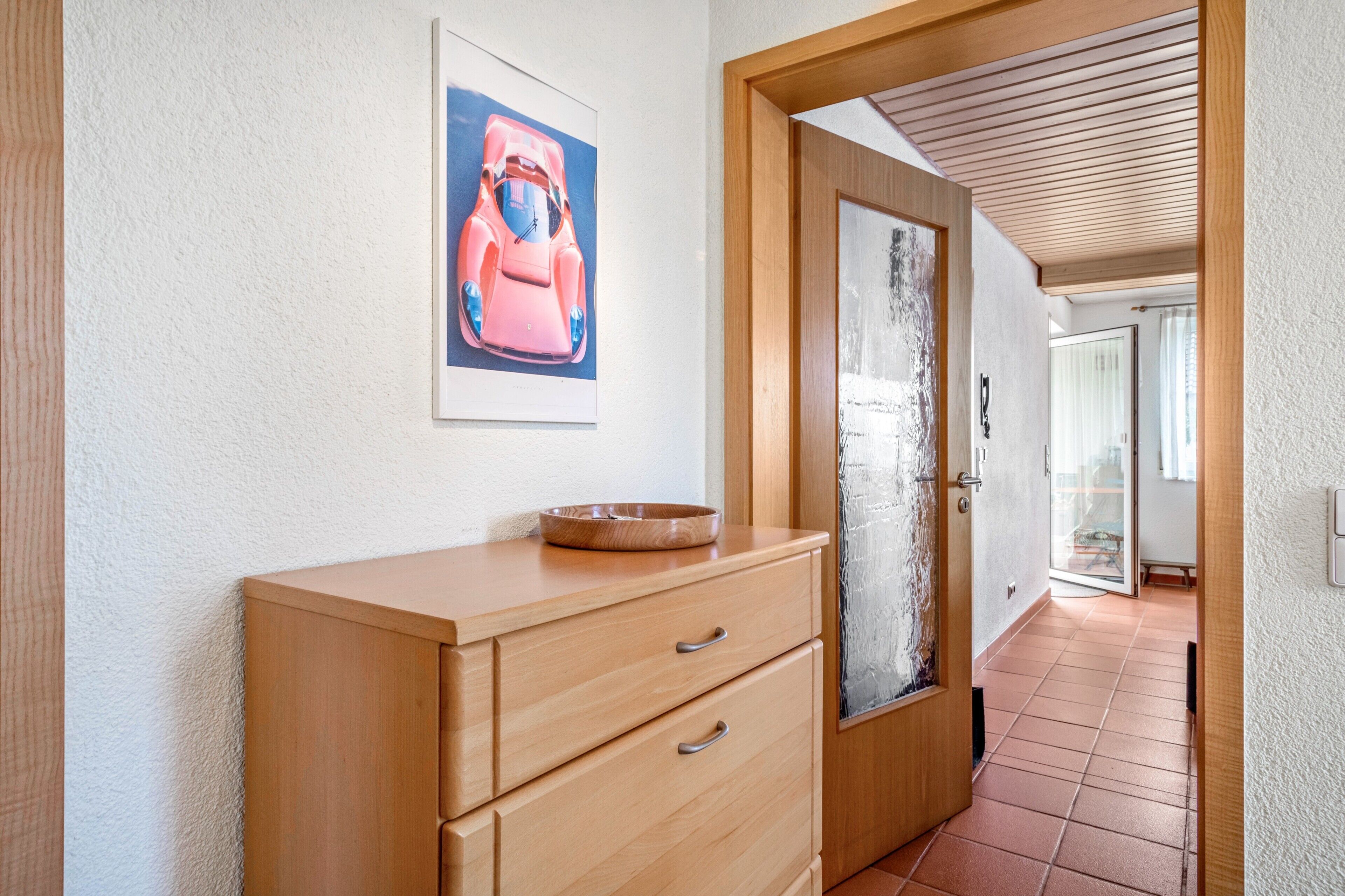 A hallway with a wooden cabinet, a framed picture of a car, and a door leading to another room.