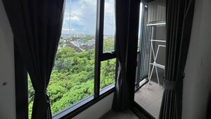 A room with large windows, a balcony, and a view of greenery and buildings.