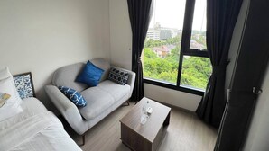 A modern hotel room with a grey sofa, a coffee table, and a large window with curtains.