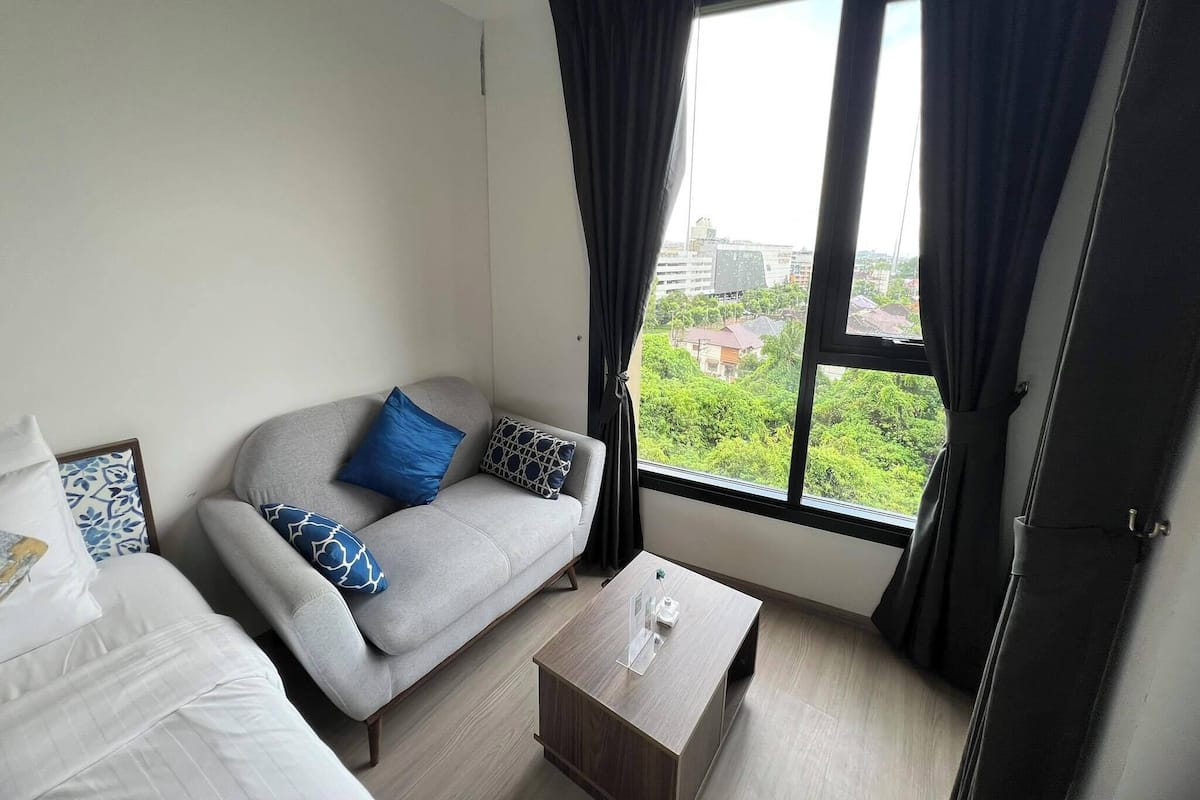 A modern hotel room with a grey sofa, a coffee table, and a large window with curtains.