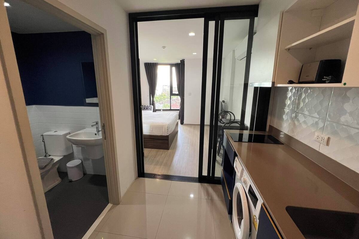 A modern hotel room with a bathroom, a bed, a kitchen area, and a view of the outside.