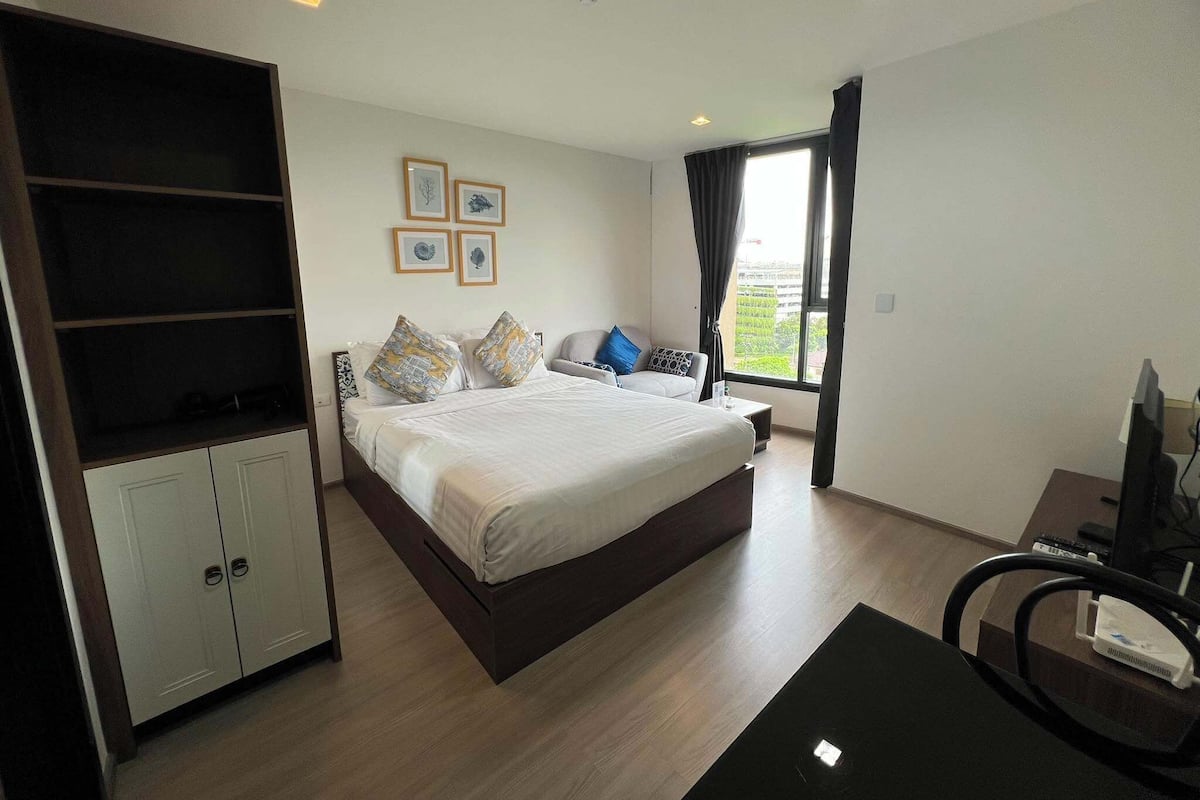 A bedroom with a bed, a wardrobe, a desk with a computer, and a window with curtains.