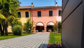 A building with a paved entrance, arched doorways, and a garden with various plants and flowers. - Casa Lilla - House with Garden near Venice (Veneto)