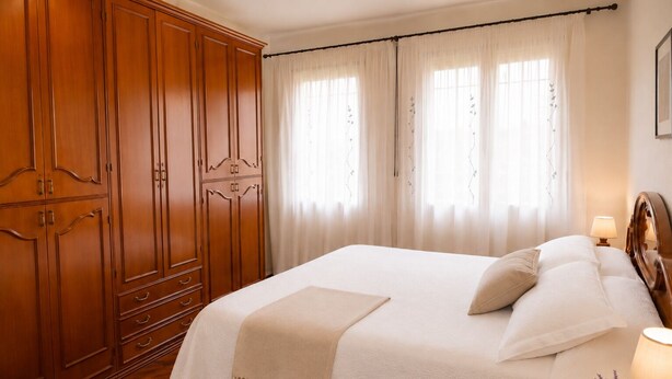 A bedroom with a large wooden wardrobe, a bed with white bedding, and a window with sheer curtains. - Casa Lilla - House with Garden near Venice (Veneto)