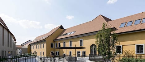 Une rangée de bâtiments jaunes, avec une cour, une clôture noire et un arbre.