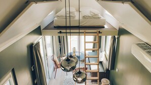 Une chambre aménagée en mezzanine avec un lit, une échelle, une table et une chaise.