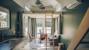Une cuisine moderne dotée d’un évier intégré, un coin repas avec une table ronde et des chaises, et une chambre en mezzanine accessible par une échelle.