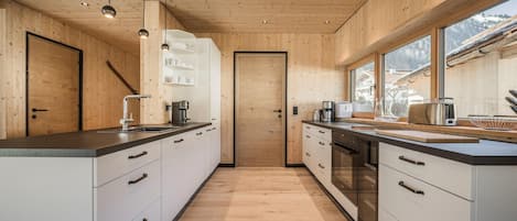 Una cocina moderna con paredes de madera y ventanas amplias, que cuenta con una isla central, armarios empotrados y electrodomésticos de acero inoxidable.