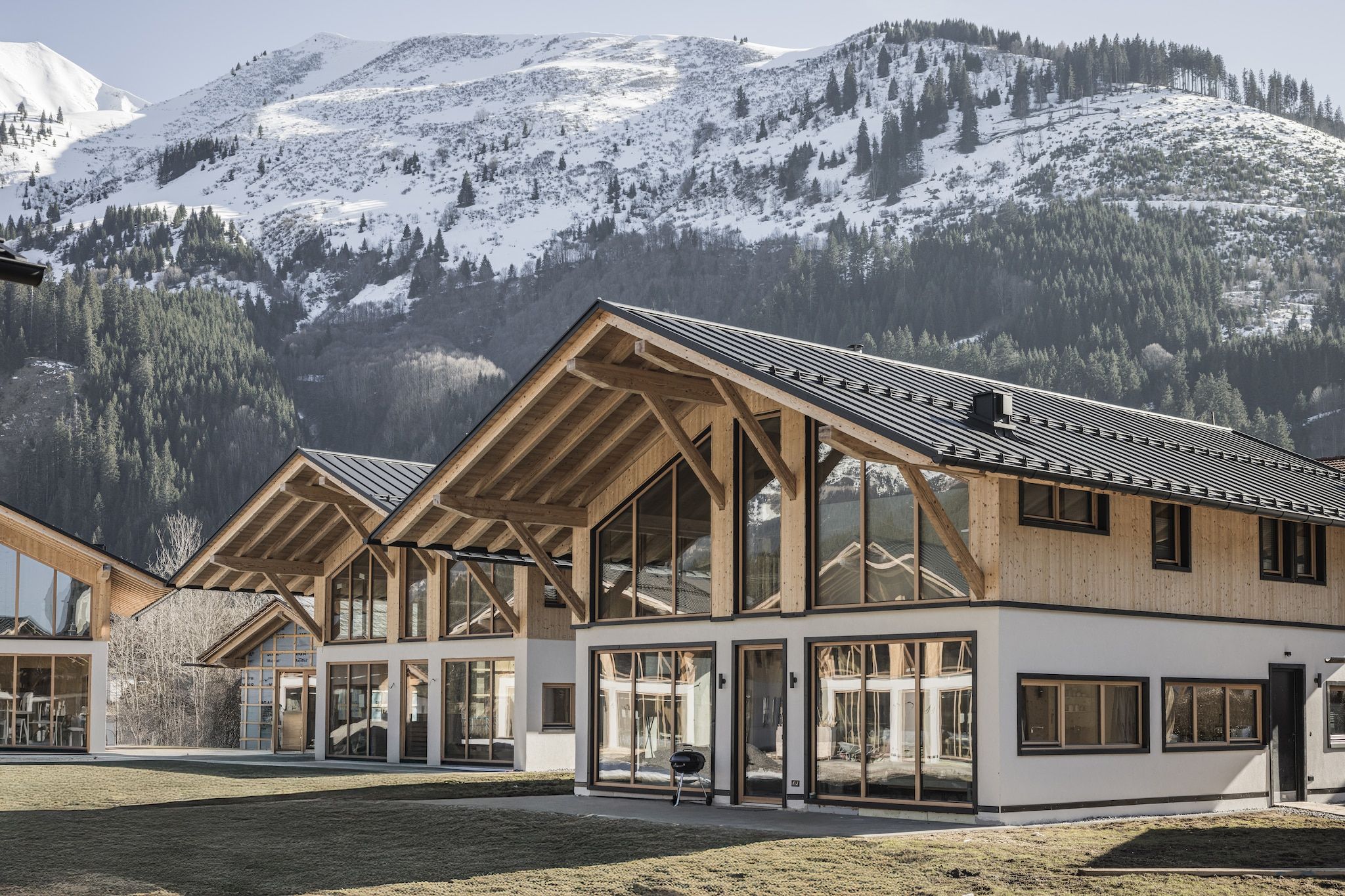 Un bâtiment moderne doté de grandes fenêtres et d’une façade en bois, qui se détache sur un paysage montagneux.