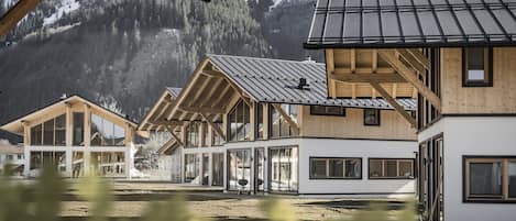 A modern building with large windows and a wooden facade, set against a mountainous backdrop.