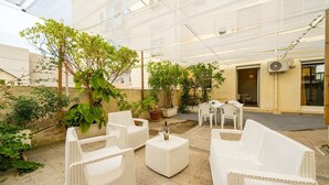 Ein Außenbereich mit Terrassenausstattung, Korbmöbeln, Pflanzkübeln und einer Konstruktion aus Glasplatten.