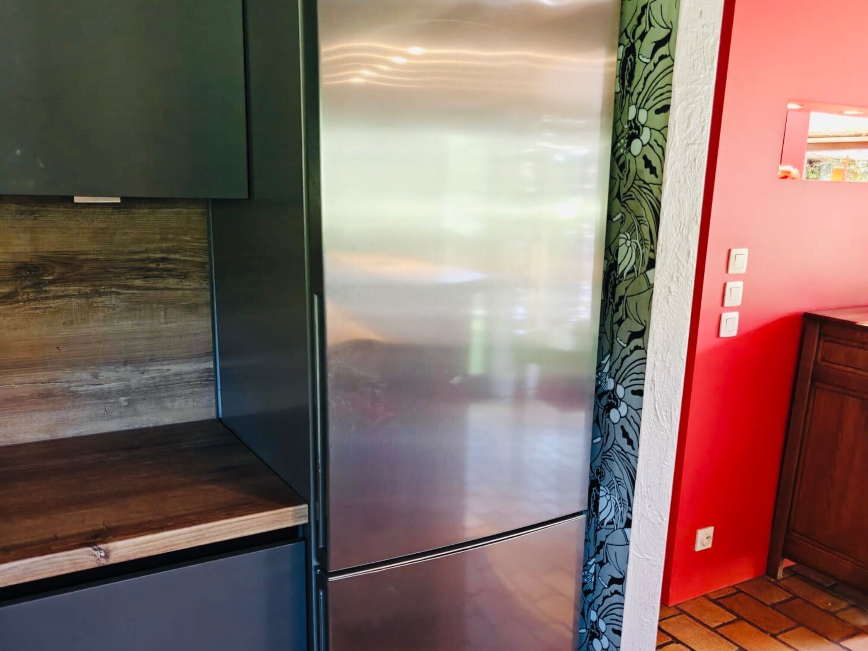 A kitchen with a stainless steel refrigerator, wooden cabinets, and a red wall.