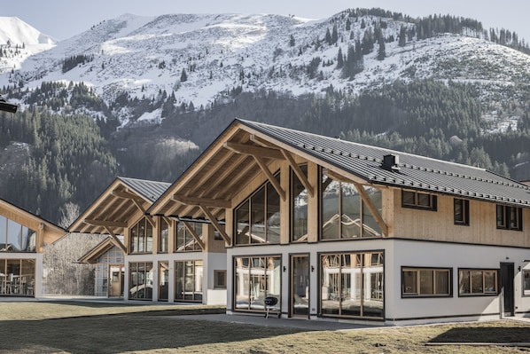 A modern building with large windows and a wooden facade, set against a mountainous backdrop.