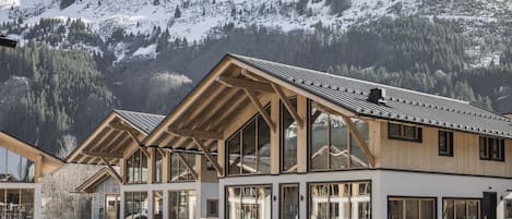 A modern building with large windows and a wooden facade, set against a mountainous backdrop.