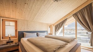 Een houten slaapkamer met een bed, een bankje, een driepootlamp en een raam met gordijnen.