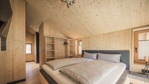 Een slaapkamer met houten lambrisering, een groot bed, inbouwkasten en een raam met zonwering.