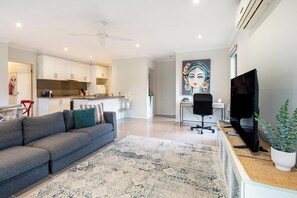 Ein modernes Wohnzimmer mit einer Couch, einem Fernseher, einem Schreibtisch und einem Gemälde an der Wand.