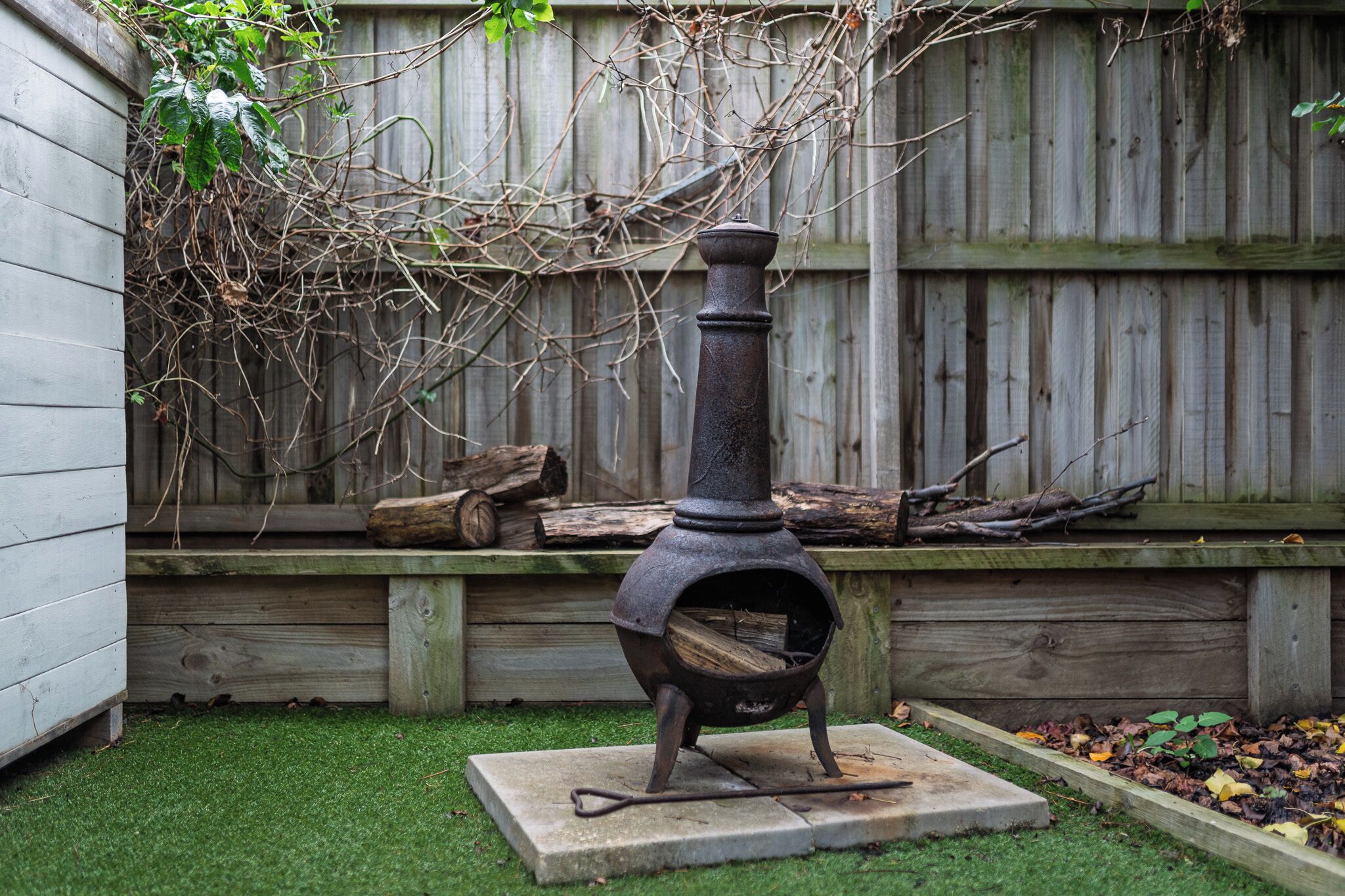 A wood-burning stove in a backyard with a wooden fence and a grassy area.