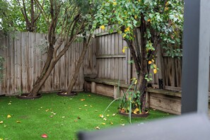 Ein Garten mit Holzzaun, Bank und Baum mit gelben Blüten.