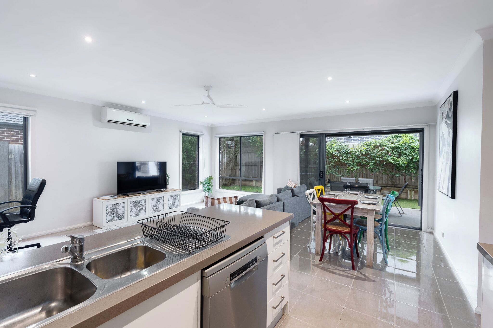 A modern kitchen with a dishwasher, a TV, and a dining area with a table and chairs.