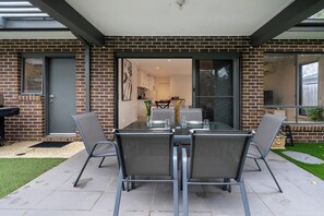 A patio with a table and chairs, a brick wall, and a sliding glass door leading to an interior space. - Seabreeze at Oakdean, Pet-Friendly (Ocean Grove)