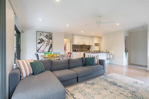 A modern living room with a gray sectional sofa, a patterned rug, and a dining area with colorful chairs. - Seabreeze at Oakdean, Pet-Friendly (Ocean Grove)