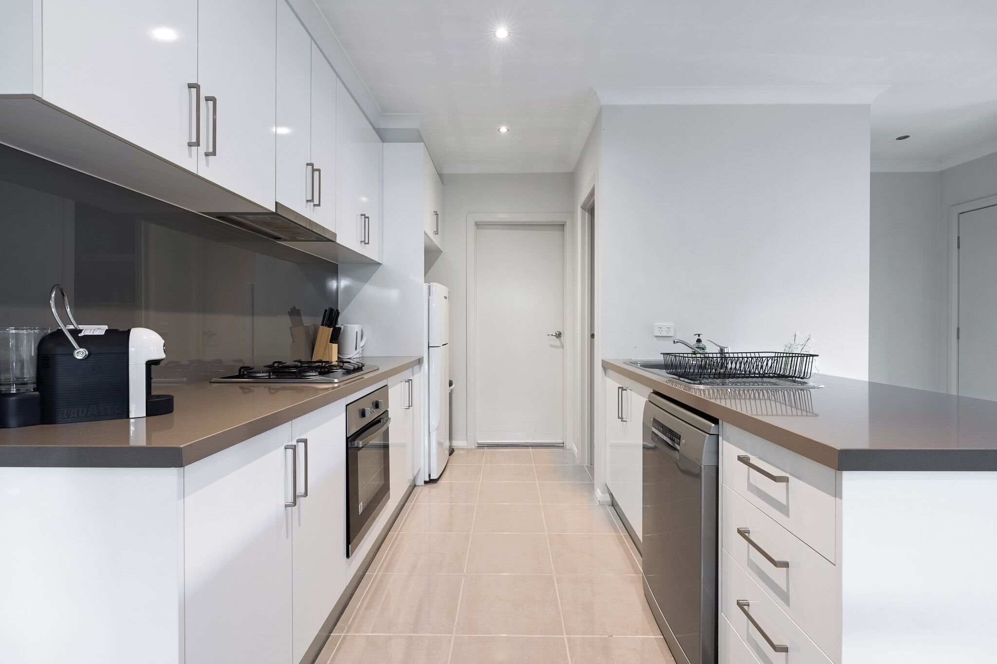 A modern kitchen with white cabinets, stainless steel appliances, and a tiled floor.