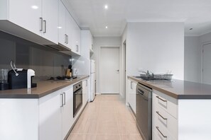 A modern kitchen with white cabinets, stainless steel appliances, and a tiled floor. - Seabreeze at Oakdean, Pet-Friendly (Ocean Grove)