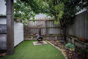 Ein Garten mit Kaminofen, Kunstgrasanlage, Holzzaun und einem Baum.
